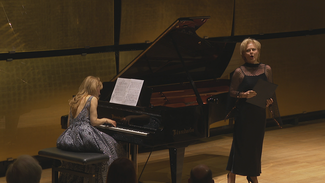 Eine Dame sitzt am Klavier und eine andere singt für das Publikum 