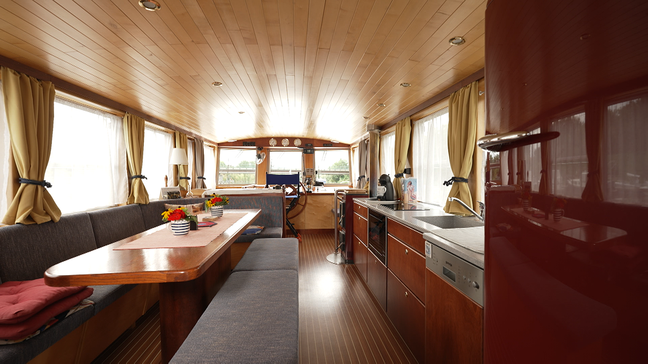 Der Innenraum eines Hausbootes, mit großem Essbereich, rotem Kühlschrank, Küche, Holzvertäfelung und dem Steuerrad