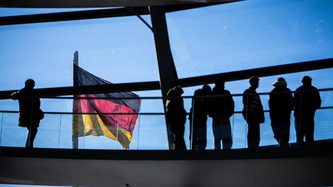 Besucher gehen vor der Deutschlandflagge in der Kuppel im Bundestag