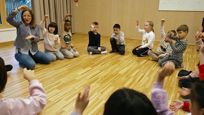 Musikschulkinder sitzen mit Lehrerin im Kreis und singen und gestikulieren
