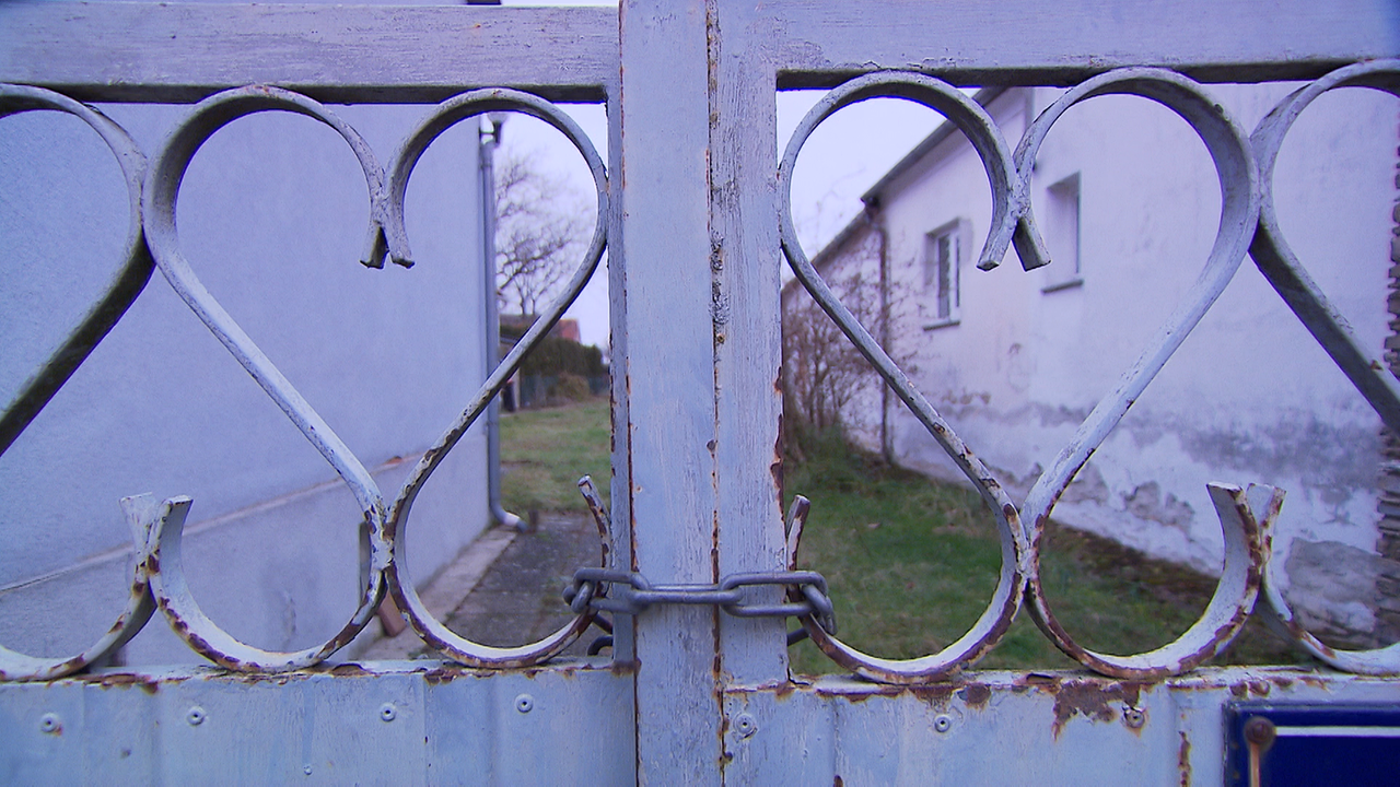 Ein rostiges Tor, dahinter ein kleiner grüner Streifen zwischen zwei Häusern.
