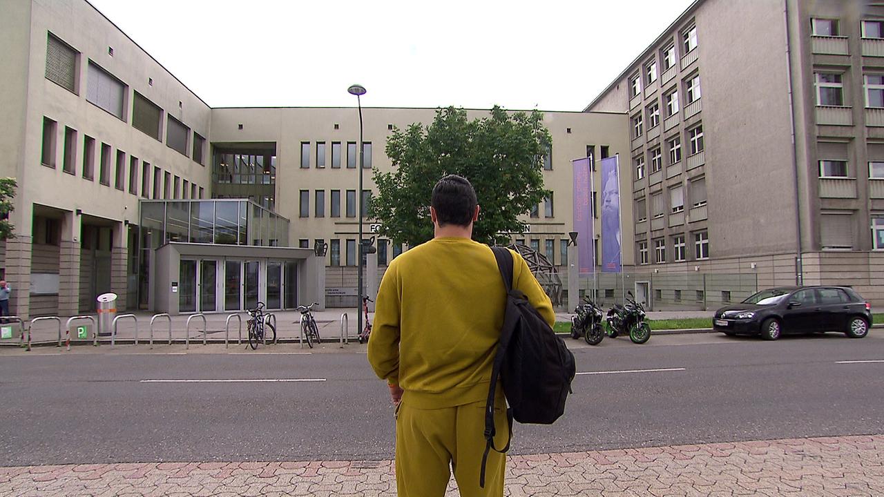 Der ehemalige HTL-Schüler, in Jogginghose gekleidet, steht vor dem HTL-Schulgebäude 