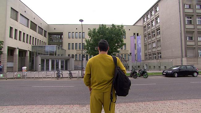 Der ehemalige HTL-Schüler, in Jogginghose gekleidet, steht vor dem HTL-Schulgebäude 