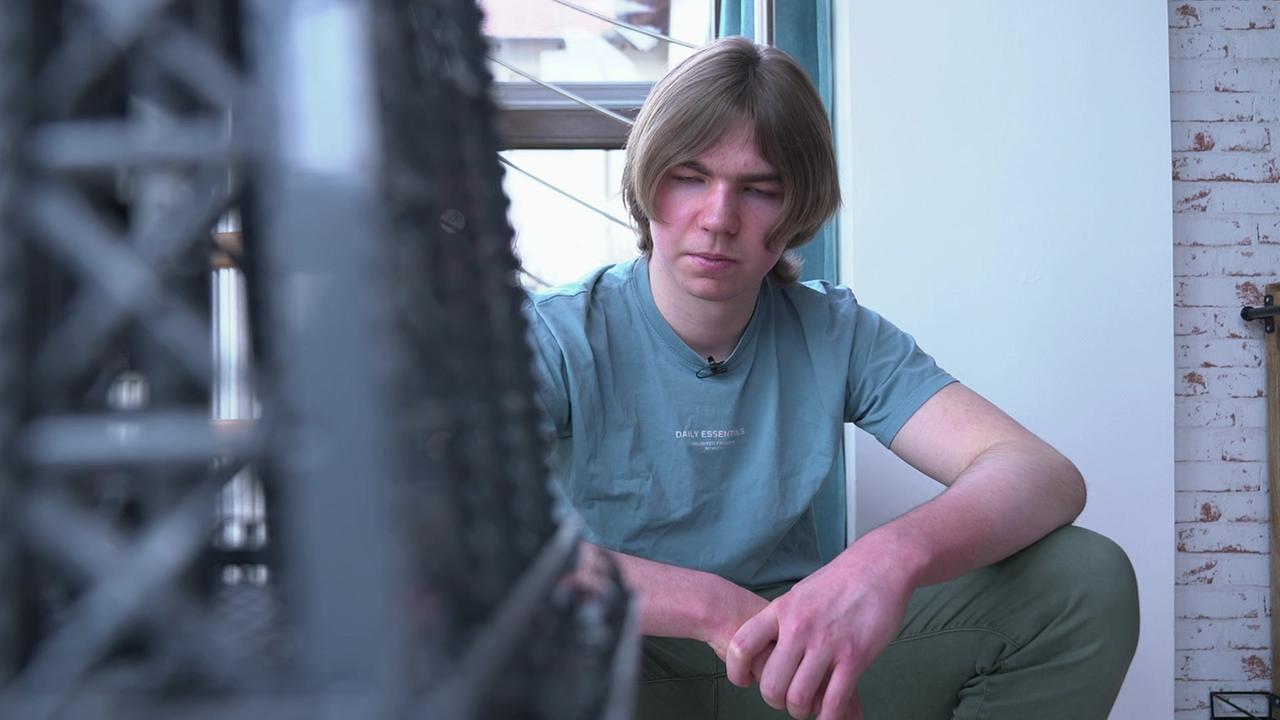 Man sieht den jungen Mann sitzend hinter einem von ihm gebauten Objekt sitzen