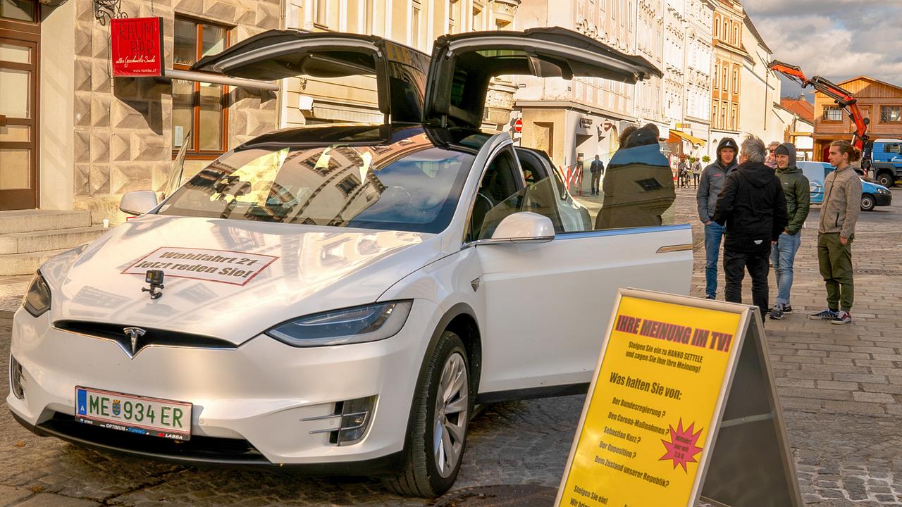 Ein weißer Tesla mit nach oben aufklappbaren Türen steht geparkt vor einer Häuserzeile.
