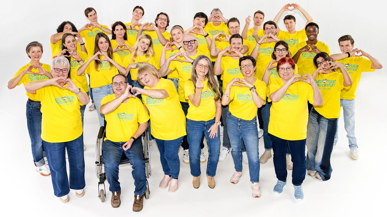 Mehrere Volunteers mit gelben T-Shirts mit der Aufschrift „Eurovision Song Contest“ strahlen freundlich in die Kamera