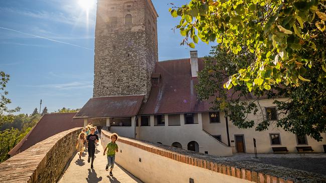 © Kultur-Betriebe Burgenland Ein paar Kinder laufen aus der Burg Schlaining heraus. Hinter dem Burgturm blinzelt die Sonne hervor.