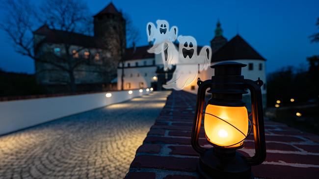 © Kultur-Betriebe Burgenland Zu sehen ist die Burg Schlaining bei Nacht. Davor fliegen zwei Gespender. Eine Laterne steht auf einer Mauerbank.