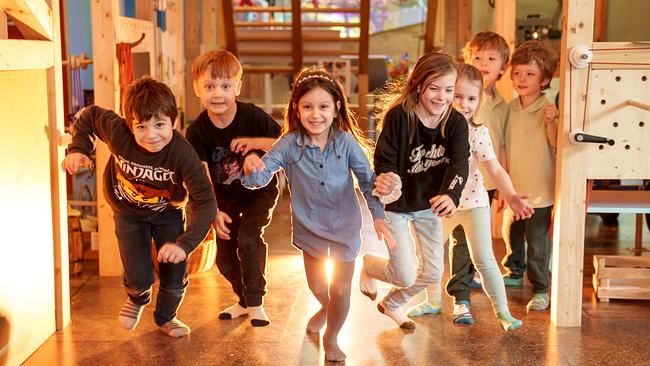 Im Bild: 5 gut gelaunte Kinder laufen durch das Kindermuseum, zwei stehen im Hintergrund. 