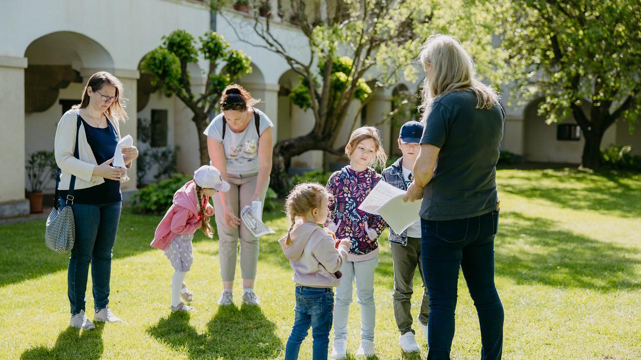 Eine Gruppe mit Kindern und Erwachsenen stehen im sonnigen Garten und studieren die Schatzkarten.