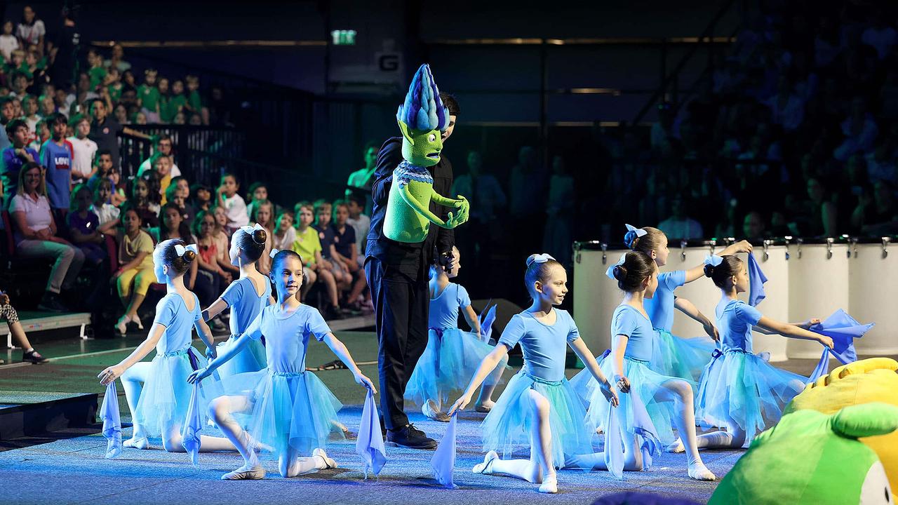 © Martin Votava Kinder aus einer Ballettgruppe führen einen Tanz auf. Sie sind weiß gekleidet und knien am Boden, in der Mitte steht eine Grüne Figur.