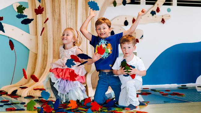 Im Bild: Drei Kinder kniehen neben einem Holbaum und spielen mit Blättern aus Filz. 