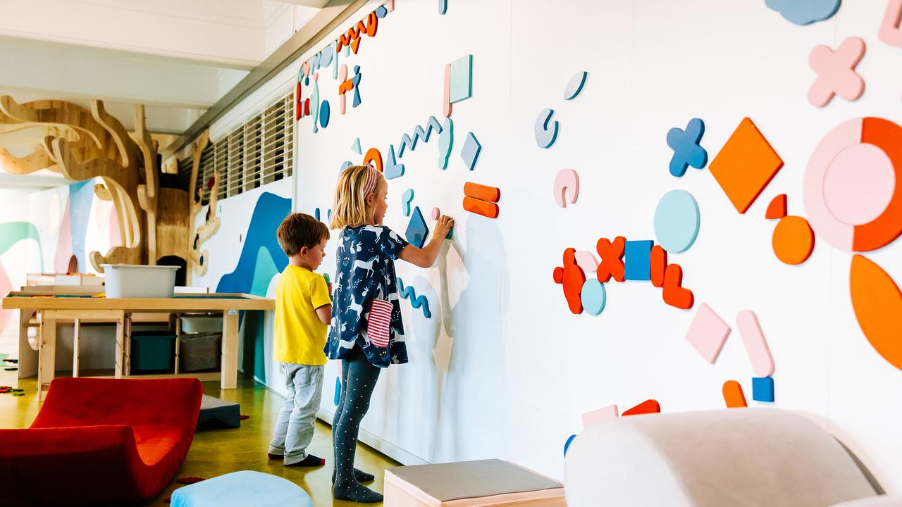 Im Bild: Ein Bub und ein Mädchen stehen vor einer weißen, magnetischen Wand und gestalten Muster aus bunten Magneten. 