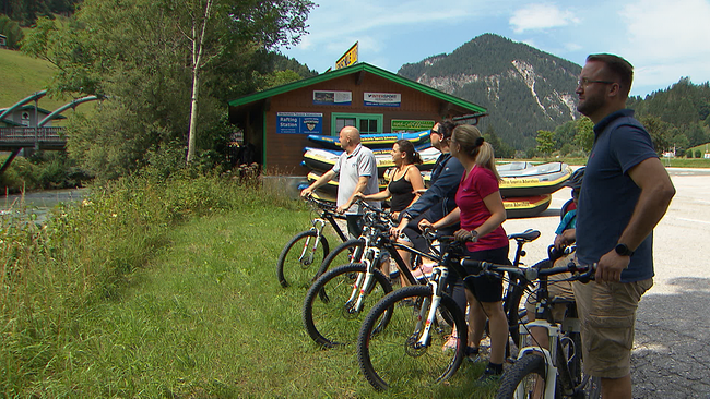 Fünf Radfahrer vor einer Hütte, Bergkulisse im Hintergrund