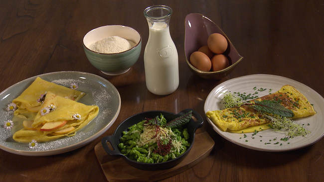 Schalen und Flasche auf einem Tisch, gefüllt mit Eiern, Mehl und Milch. Davor drei Gerichte aus diesen Zutaten