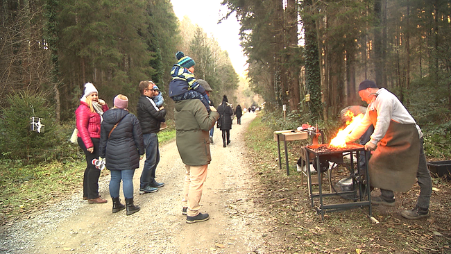 Spaziergänger auf Waldweg, rechts im Bild Aussteller mit offenem Feuer