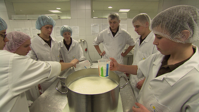 Sieben Studierende stehen - weiß gekleidet - um einen großen Topf mit Milch