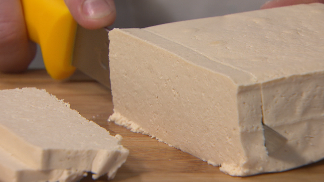 ein Tofu-Block wird mit einem großen Messer in Scheiben geschnitten