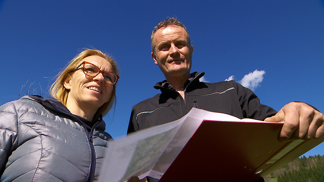 Zwei Menschen stehen mit Mappe nebeneinander, im Hintergrund blauer Himmel
