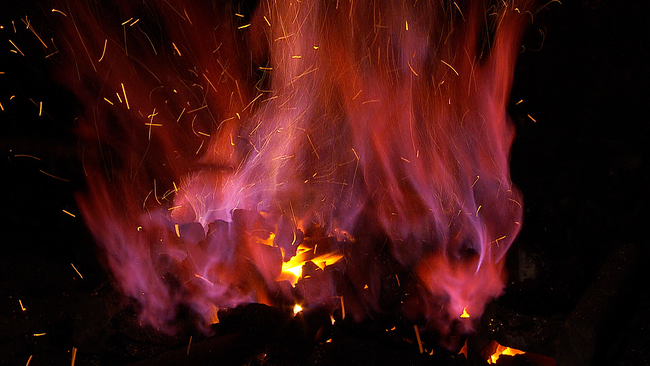 glühende Holzkohle im Feuer, das rot schimmert und gelbe Funken spritzt