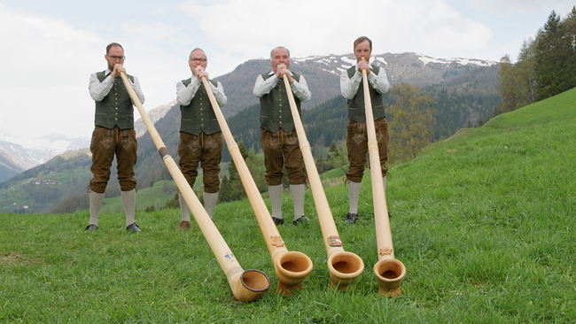 Vier Menschen in Lederhosen auf Almwiese mit 4 Alphörnern