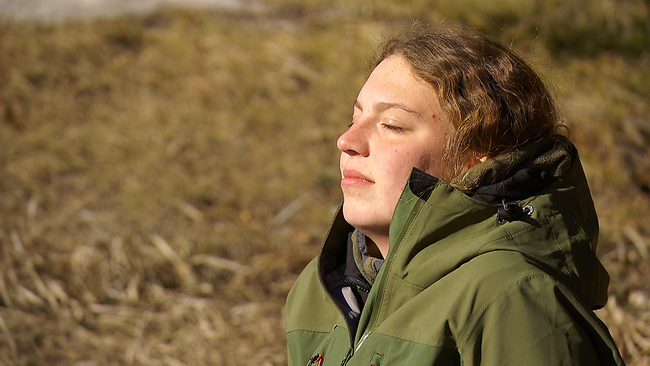 Eine junge Frau, die ihr Gesicht mit geschlossenen Augen zur Sonne richtet und die fische Winterluft genießt