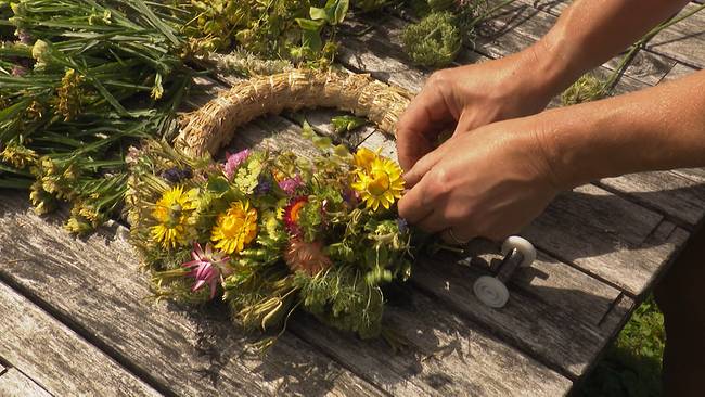 © ORF NÖ Zwei Hände binden einen bunten Blumenkranz