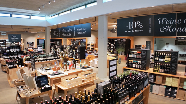 Innenansicht eines Lokals mit vielen Regalen und Thekenbereich, in denen Weine und Spezialitäten aus einer Weinregion präsentiert werden 