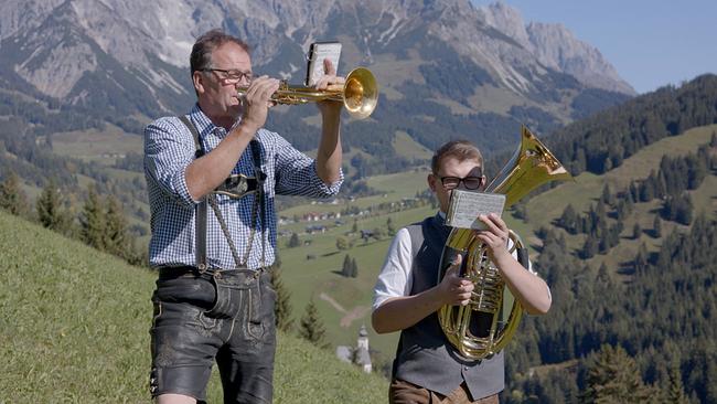 Zwei Musiker in Tracht spielen Blasmusik im Gebirge. 
