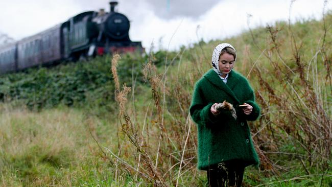 Amanda Holden (Lucy Eyelesbarrow) steht auf einer Wiese unterhalb einer Bahntrasse, auf der gerade ein Zug mit einer Dampflok herannaht. Sie hat etwas in der Hand, das sie betrachtet.
