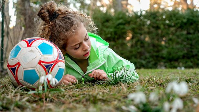 Ein Kind liegt zu Frühlingsbeginn in der Wiese und freut sich über Knospen, Blüten und erste warme Sonnenstrahlen