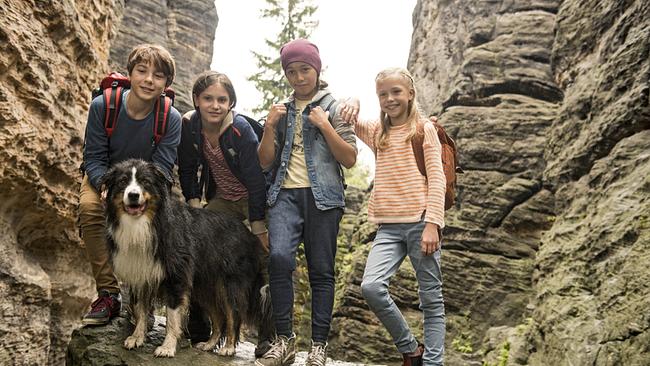 Vier Kinder und ein Hund stehen auf einem Felsvorsprung. Sie tragen Rucksäcke. 