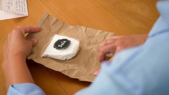 Eine Person hält eine Verpackung, auf der Verpackung liegt eine Packung Salz