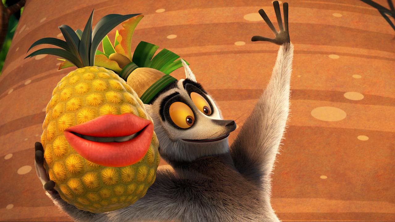 Ein Lemur hält eine große Ananas in der Pfote. Die Anananas lächelt.