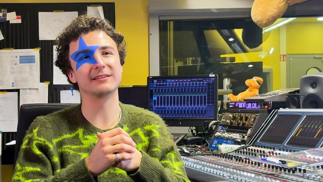 Ein junger Mann, COSMO, sitzt in einem Tonstudio. Er hat einen blauen Stern beim Auge aufgemalt.