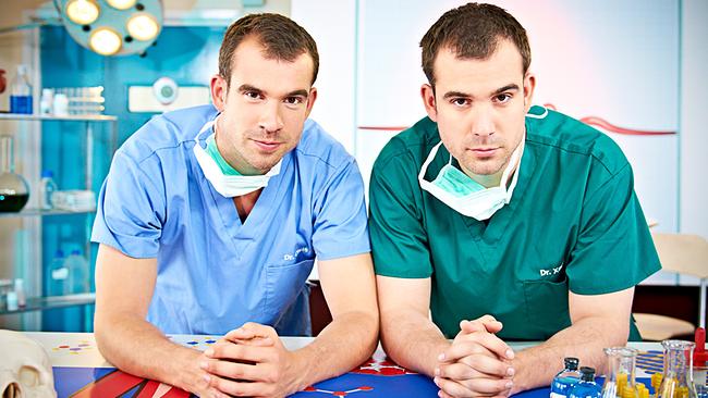 © ORF/Serious Kids Die Zwillingsärzte Chris van Tulleken (Dr. Chris), Xand van Tulleken (Dr. Xand) in Op-Kitteln und mit Masken.