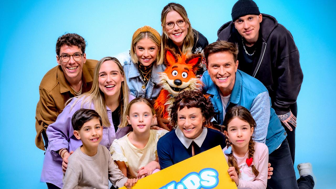Christoph Hirschler, Melanie Flicker, Fanny Stapf, Lena Großmann, Esther Csapo, Robert Steiner, Stefan Gruber mit Fuchsi und Kindern posieren vor blauem Hintergrund und halten ein Schild mit der Aufschrift „ORF Kids“.