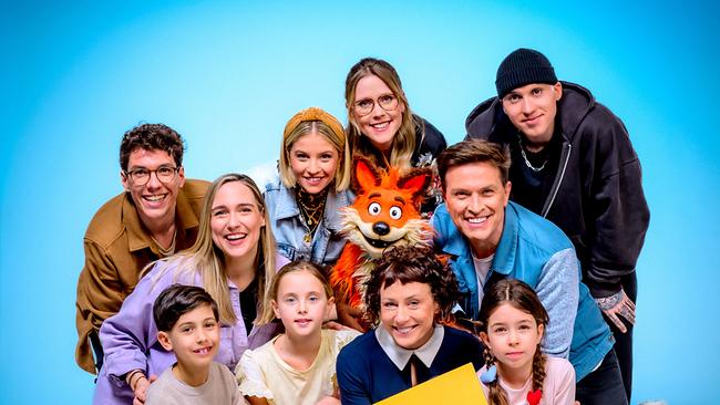 Christoph Hirschler, Melanie Flicker, Fanny Stapf, Lena Großmann, Esther Csapo, Robert Steiner, Stefan Gruber mit Fuchsi und Kindern posieren vor blauem Hintergrund und halten ein Schild mit der Aufschrift „ORF Kids“.