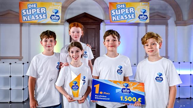 Fünf Kinder lächeln ins Bild. Ein Junge hält einen großen Gutschein in der Hand. Sie sind die Gewinner der Superklasse.