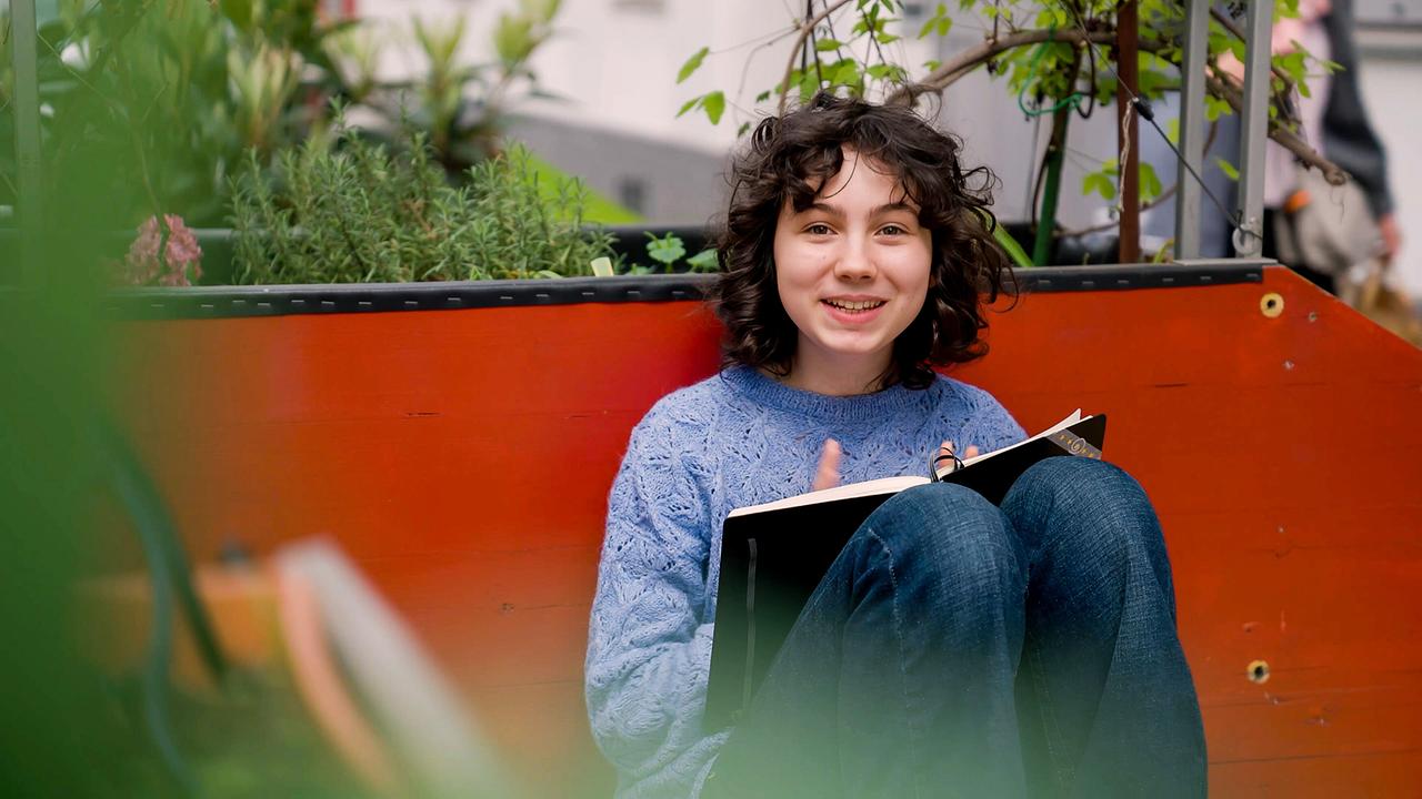 © ORF/JewelLabs Pictures Carmen Diego sitzt am Boden mit angewinkelten Beinen, sie liest ein Buch.
