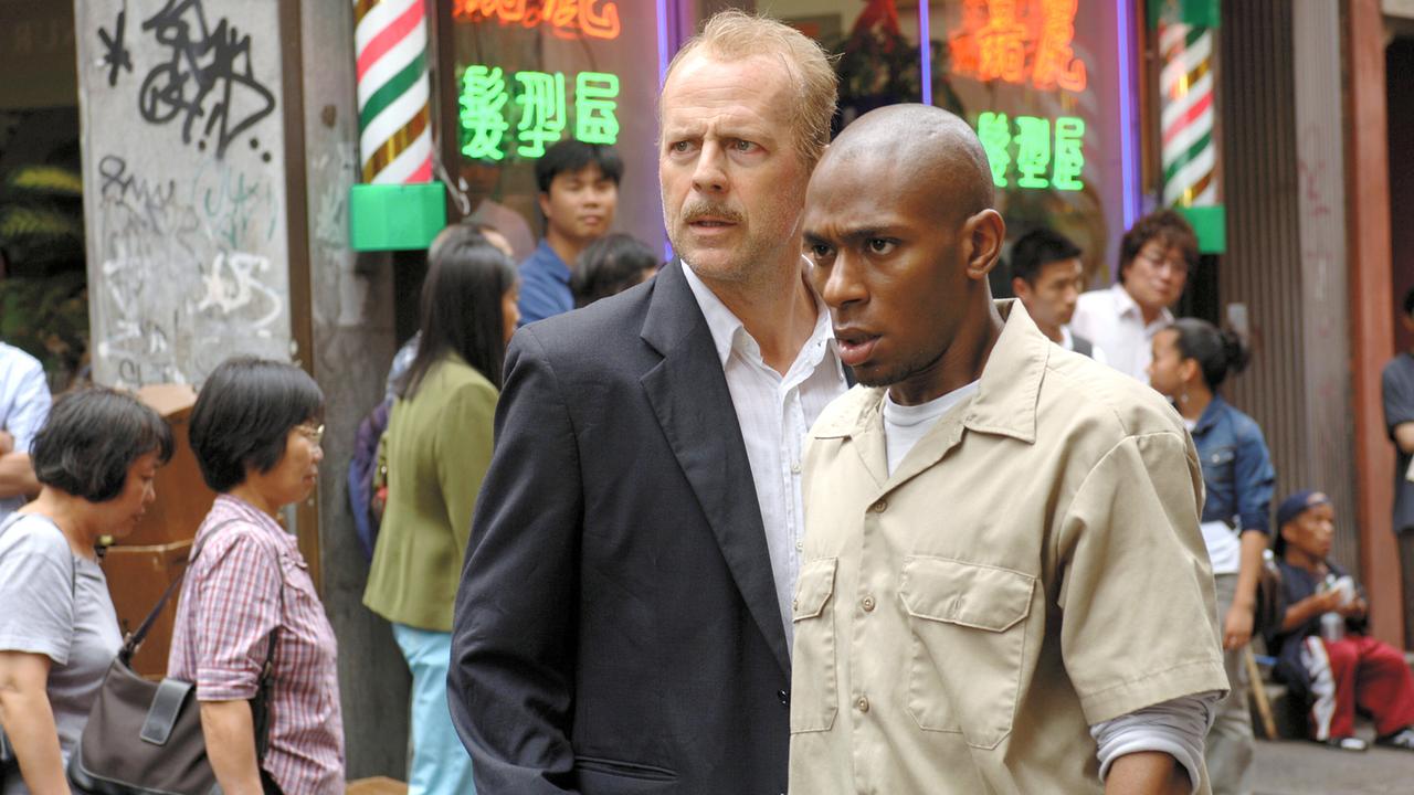 Bruce Willis als Jack Mosley mit Schnurrbart und Mos Def als Eddie Bunker auf einer Straße, hinter ihnen Menschen, in den Auslagen der Geschäften leuchten asiatische Schriftzeichen