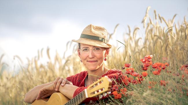 Die Kabarettistin Martina Schwarzmann sitzt mit einer Gitarre auf dem Schoß und Strohhut auf dem Kopf in einem Weizenfeld 