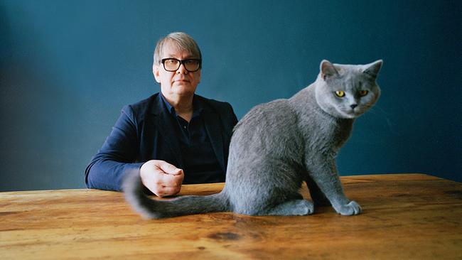 Der Autor und Musiker Sven Regener sitzt hinter einem hellen Holztisch, auf dem Tisch vor ihm sitzt eine graue Katze