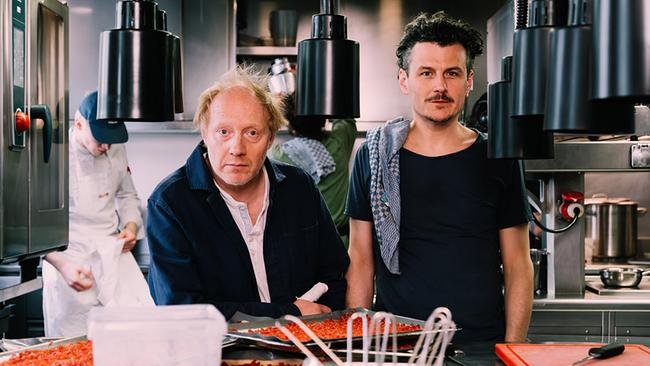 © Bild: Ingo Pertramer Die beiden Schauspieler und Podcaster Simon Schwarz und Manuel Rubey stehen in einer Gastroküche; Manuel Rubey hat ein kariertes Geschirrtuch überdie rechte Schulter geworfen und Simon Schwarz trägt einen Verband am rechten Daumen