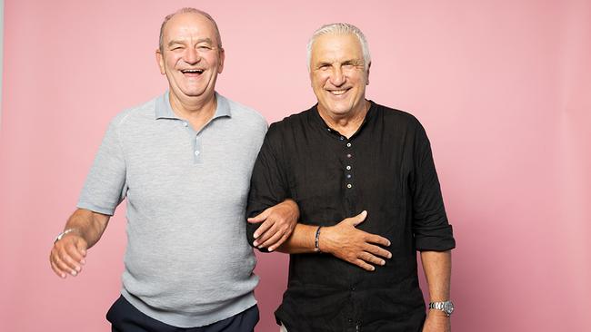 Die österreichischen Fußball-Legenden Herbert Prohaska und Hans Krankl stehen, die Arme eingehakt, vor einer rosa Wand. Sie lachen herzlich in die Kamera