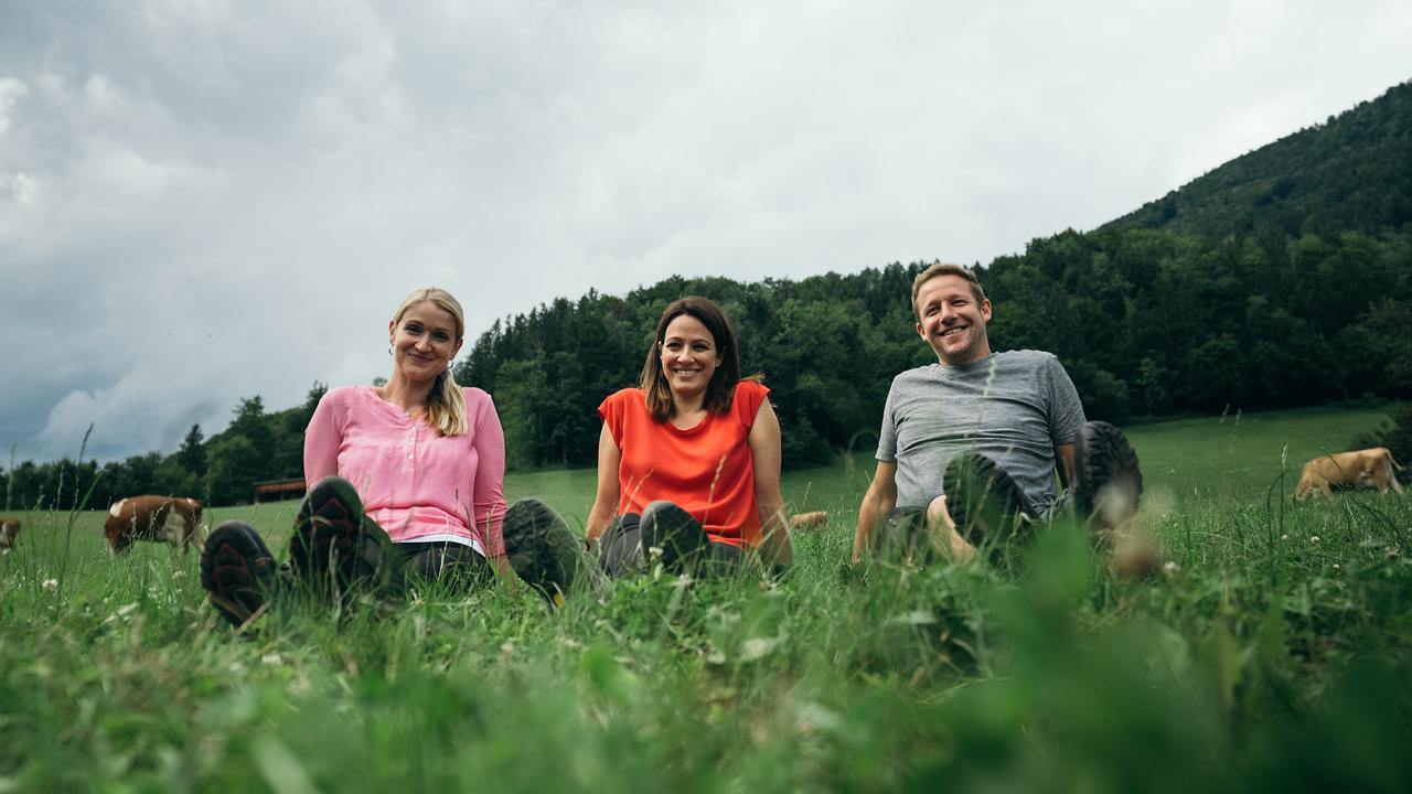 Lisa Gadenstätter sitzt mit Familie Aschauer auf einer Almwiese