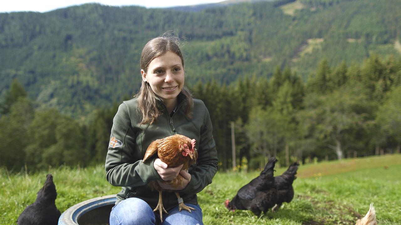 Landwirtin Sarah Stromberger sitzt draußen mit einem Huhn im Arm