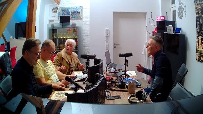 Walter "Waldi" Lehnertz sitzt mit Detlev Kümmel, Manuel Zeh und einer älteren Dame rund um einen großen Tisch. Lehnertz, Kümmel und Zeh haben Mikrofone vor sich, ein Podcast wird produziert.