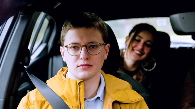 © ORF/KGP Filmproduktion Der Fahrlehrer Florian mit Brille und gelber Jacke sitzt angeschnallt am Beifahrersitz im Auto, hinter ihm lächelt Lola auf der Rückbank.