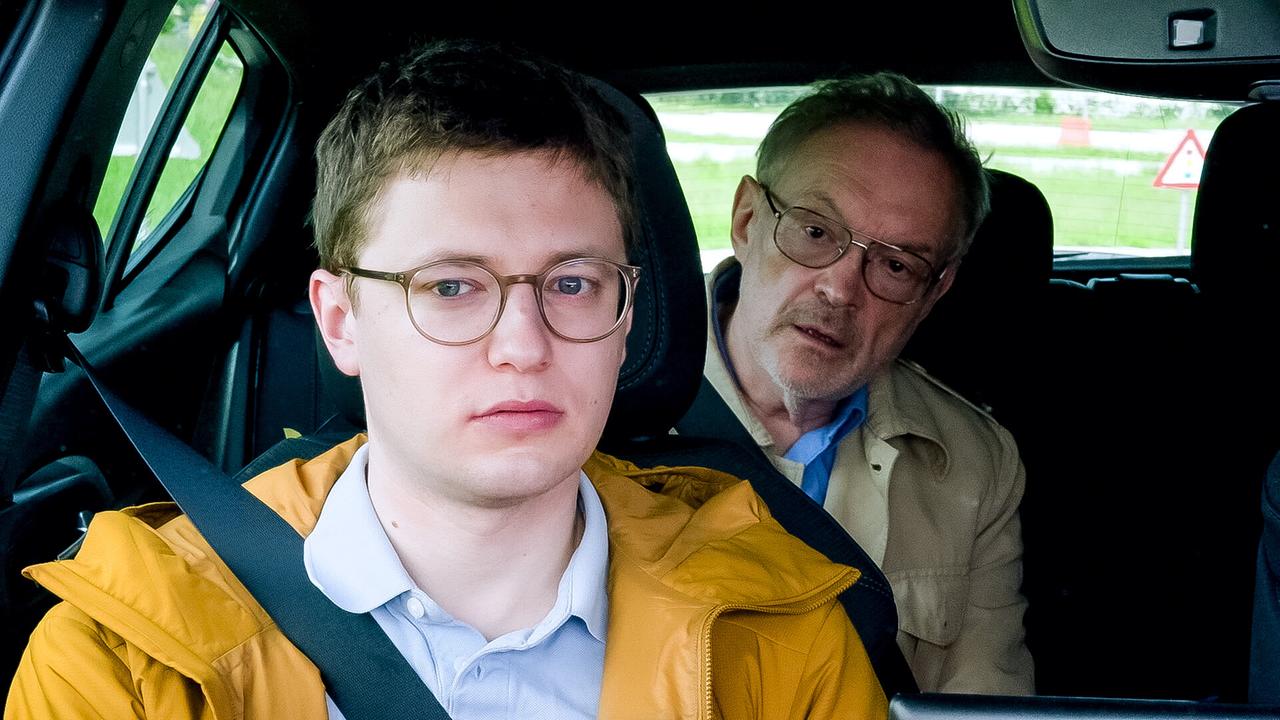 © ORF/KGP Filmproduktion Fahrlehrer Florian mit Brille und gelber Jacke sitzt angeschnallt im Auto, während Josef Hader als Fahrprüfer mit Brille sich von der Rückbank zu ihm nach vorne beugt.